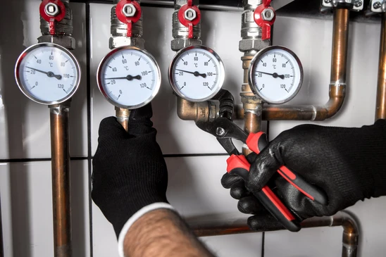 Technicien en gants noirs effectuant une maintenance sur installation de chauffage avec clé à molette